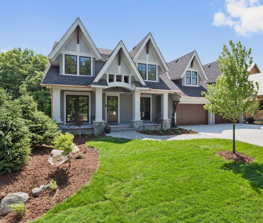 Modern two-story house with a landscaped yard, stone accents, and green trees.
